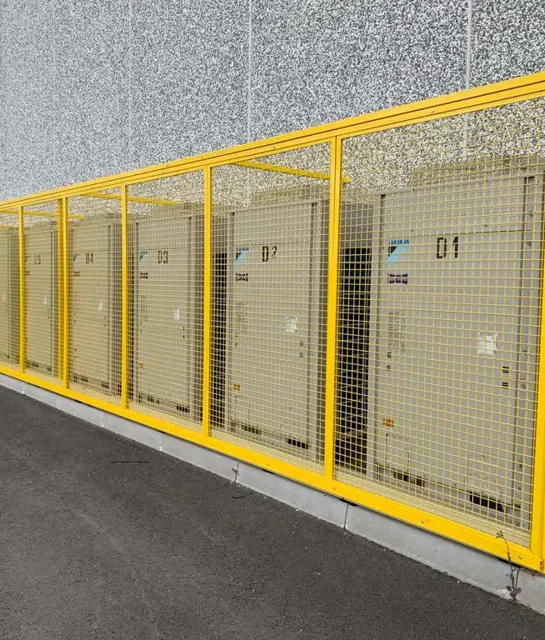 Unità esterne di climatizzatori industriali protette da recinzione di sicurezza.